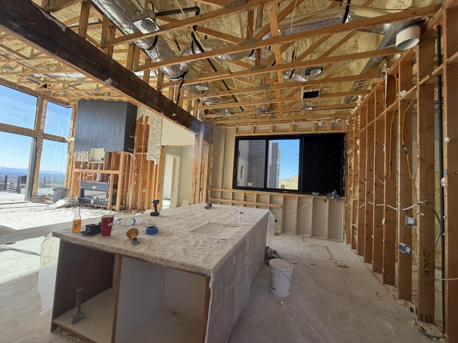 Home interior gutted to the framing and roof trusses, with the kitchen island covered in plastic sheeting