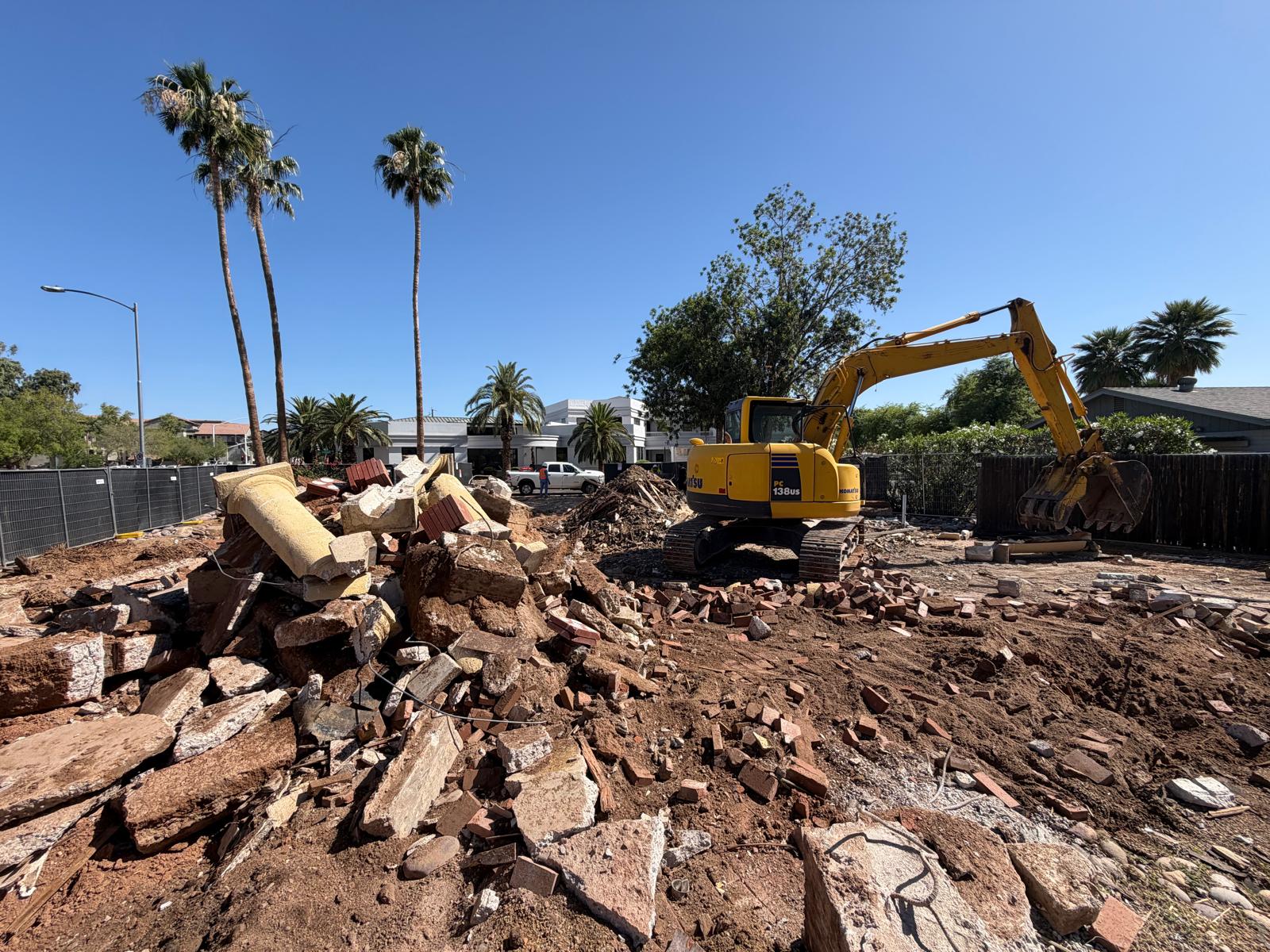 A Komatsu excavator on a cleared demolition site in Phoenix, Arizona, with broken brick and concrete rubble piled in the foreground