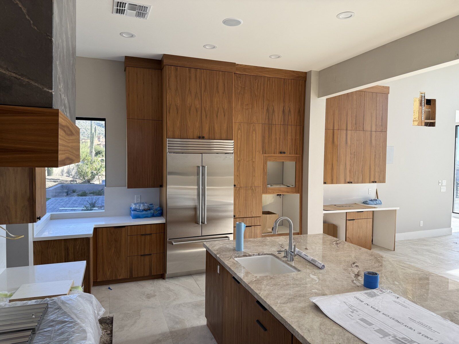 A kitchen with walnut cabinetry, a stone-topped island and a stainless refrigerator in a custom home built by Kogan LLC near Mesa, Arizona