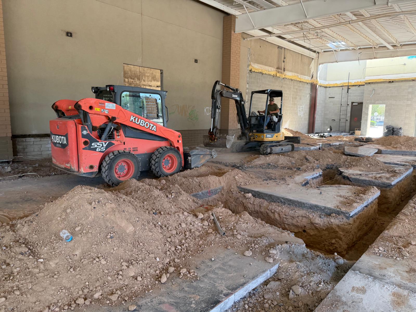 Skid steer and mini excavator breaking out a concrete slab inside a commercial building