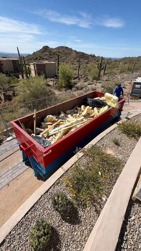 A red roll-off dumpster loaded with insulation and lumber debris on a desert hillside property in Arizona