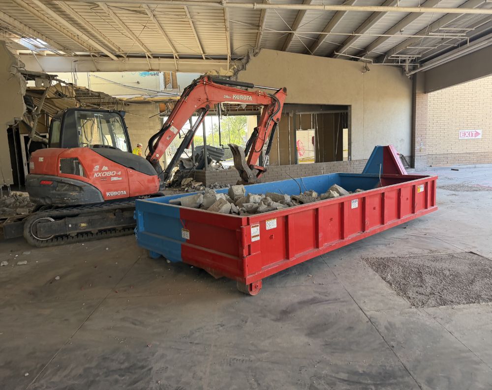 Excavator loading a dumpster during an interior industrial demolition in Phoenix