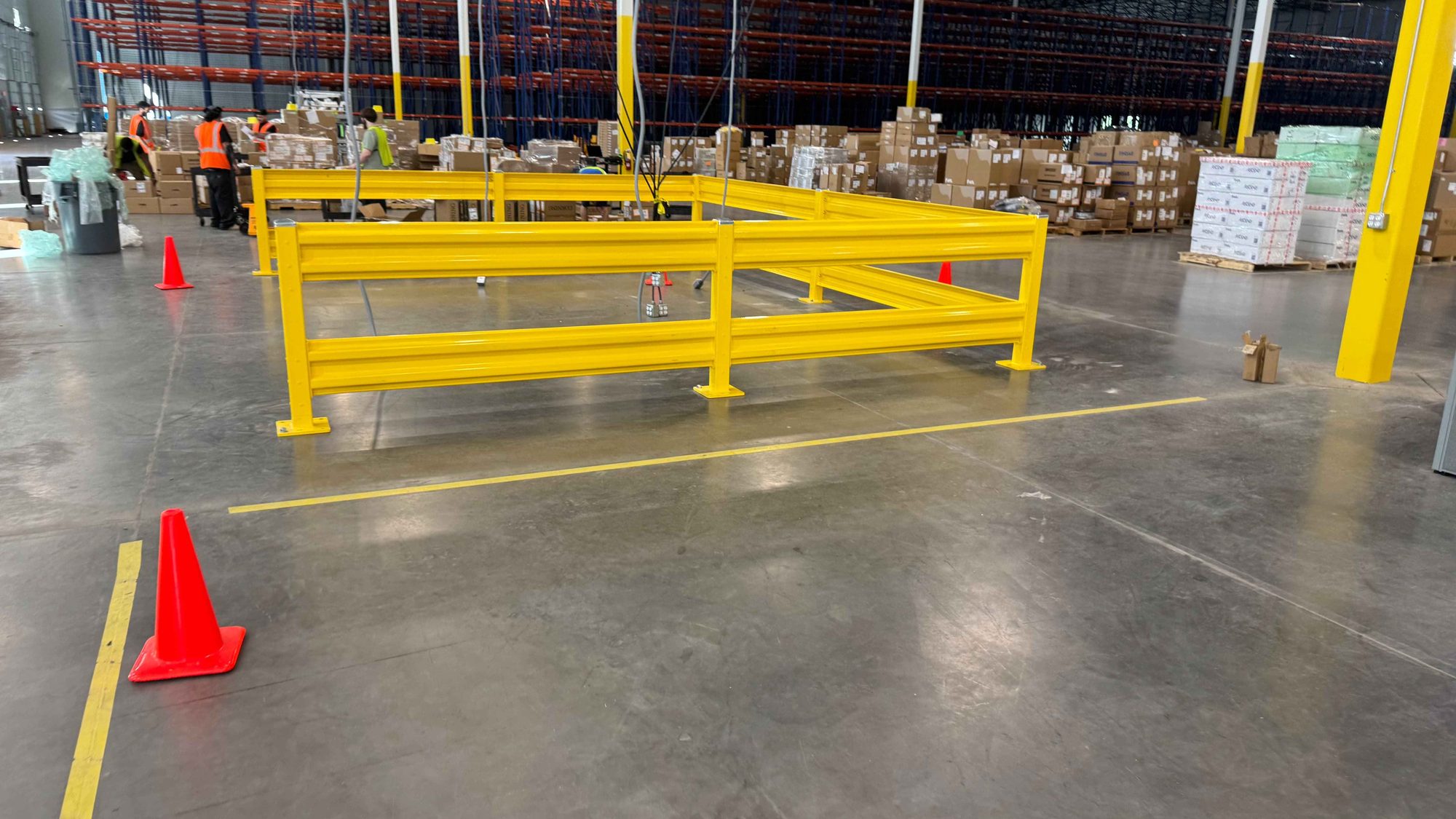 Yellow steel guardrail enclosing a work cell on a warehouse floor