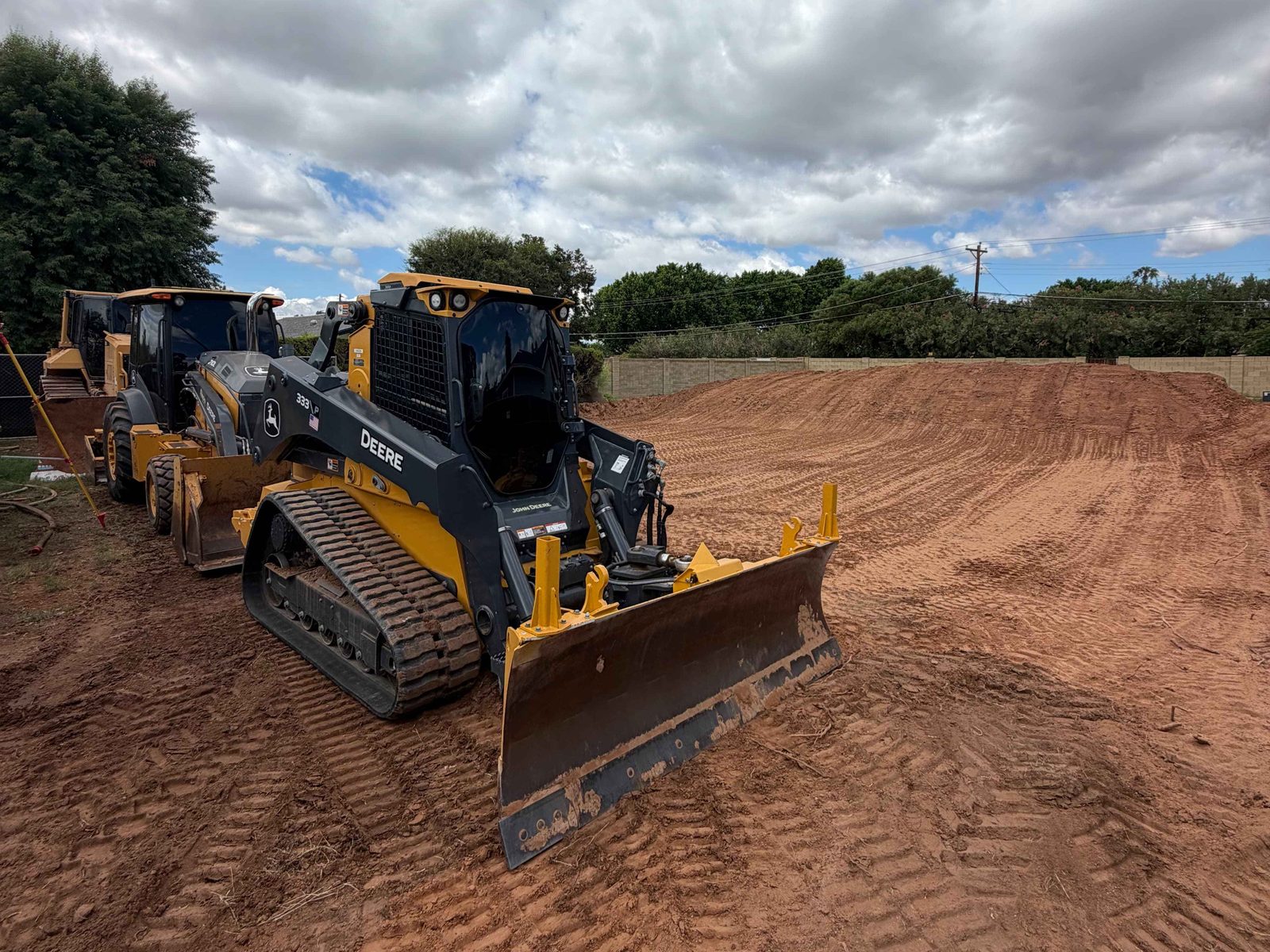 John Deere compact track loader with a dozer blade on a cleared residential lot