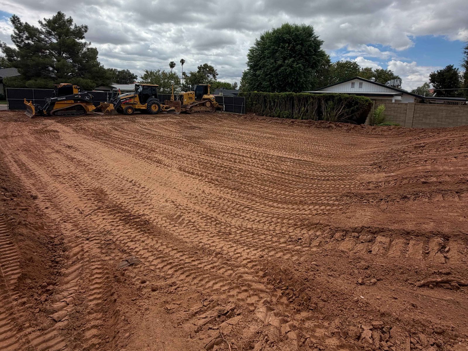 Cleared residential lot with a compact track loader, backhoe and dozer staged at the fence